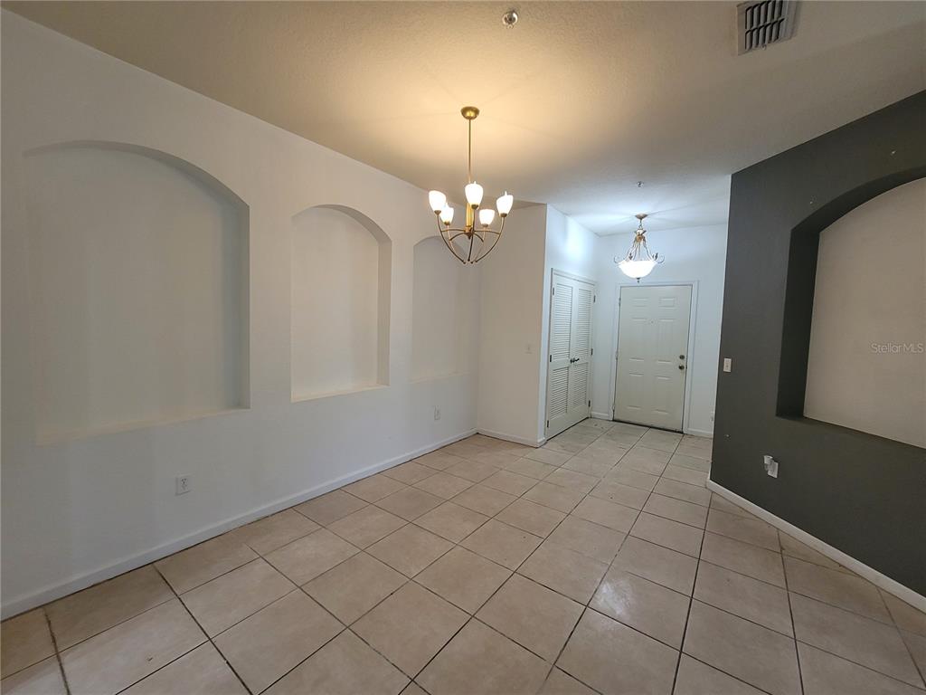 A room with tiled floors, arched wall niches, two chandeliers, and a white entry door — 3321 WHITESTONE CIRCLE UNIT 108, KISSIMMEE, FL
