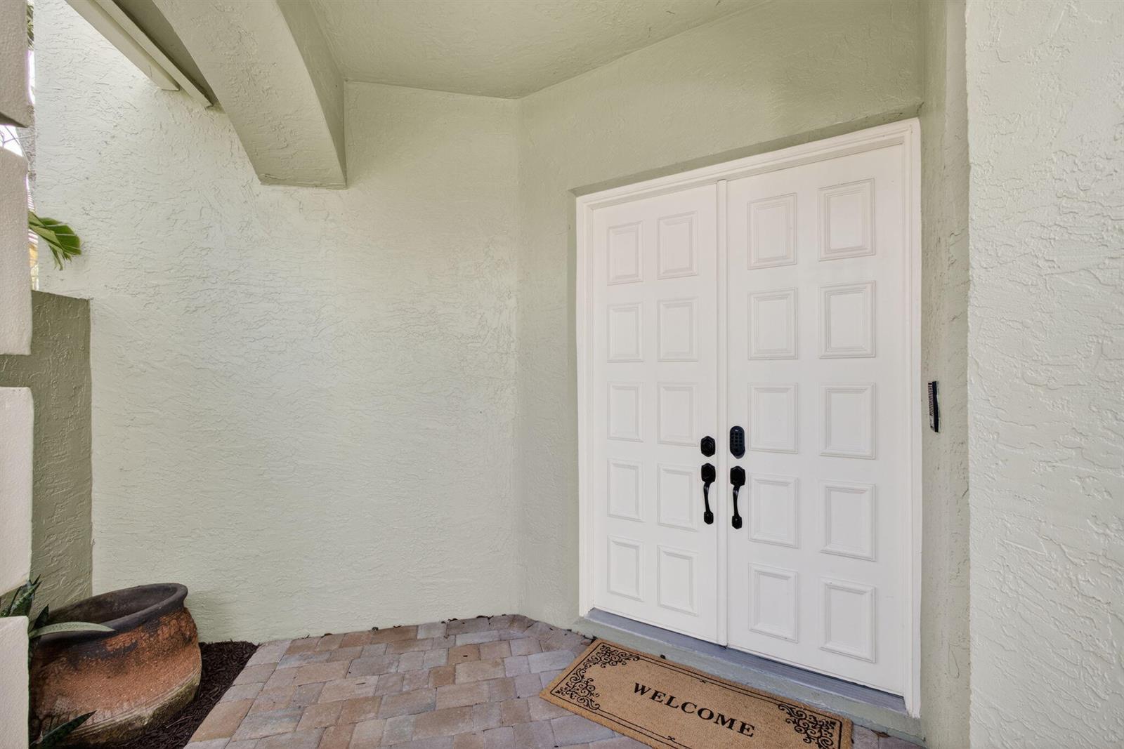 A white double front door with black hardware sits under a covered entryway with pavers — 10324 Osprey Trace, West Palm Beach FL 33412, WEST PALM BEACH, FL