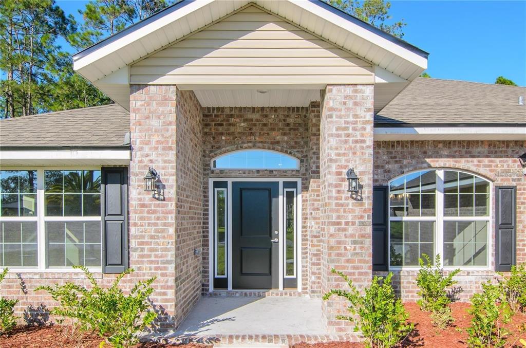 The exterior of a brick house features a covered entryway with a black front door — 98 ROLLING SANDS DRIVE, PALM COAST, FL