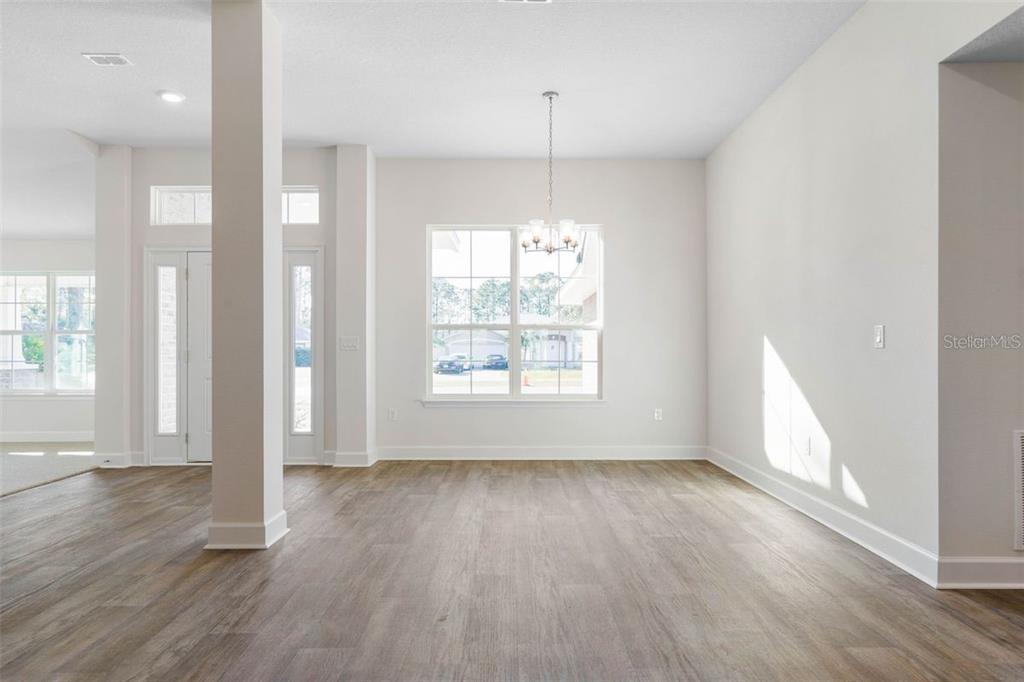An empty dining room features light-colored walls, wood-look flooring, a chandelier, and a large window — 98 ROLLING SANDS DRIVE, PALM COAST, FL