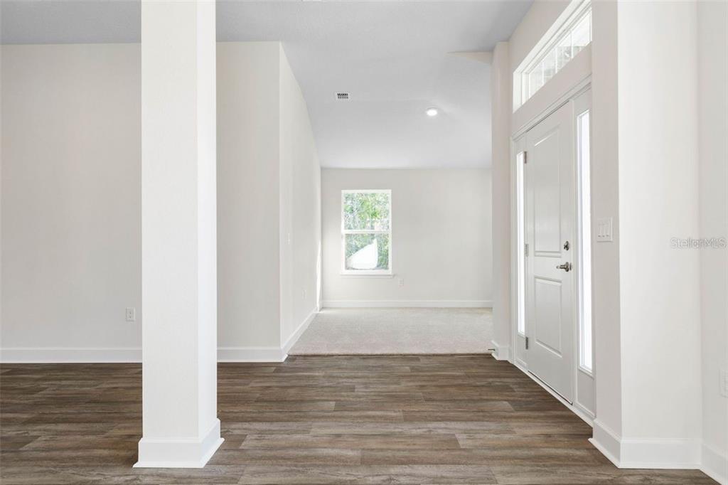 An entryway with wood-look flooring leads to a carpeted room with a single window — 98 ROLLING SANDS DRIVE, PALM COAST, FL