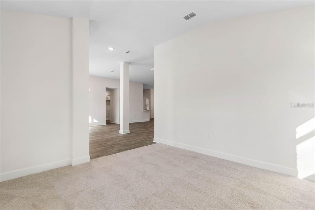 An interior view shows a carpeted room opening into a living area with wood flooring — 98 ROLLING SANDS DRIVE, PALM COAST, FL