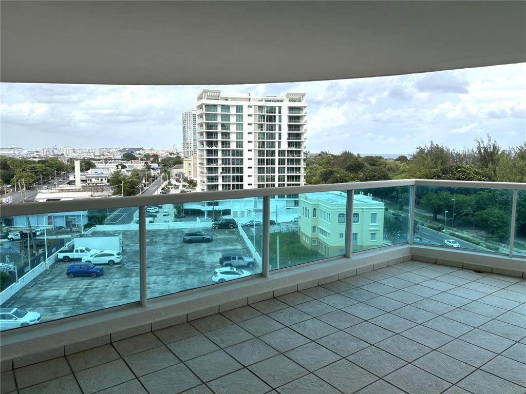 A balcony with tiled flooring and a glass railing overlooks a parking lot and buildings — 550 Avenida Constitucion AVENIDA CONSTITUCION UNIT 901, SAN JUAN, PR