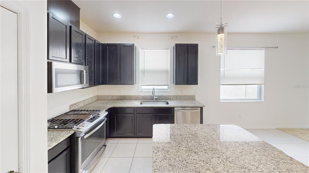 A kitchen features dark wood cabinets, granite countertops, stainless steel appliances, and tile flooring — 8331 BAYLISS COURT, ORLANDO, FL