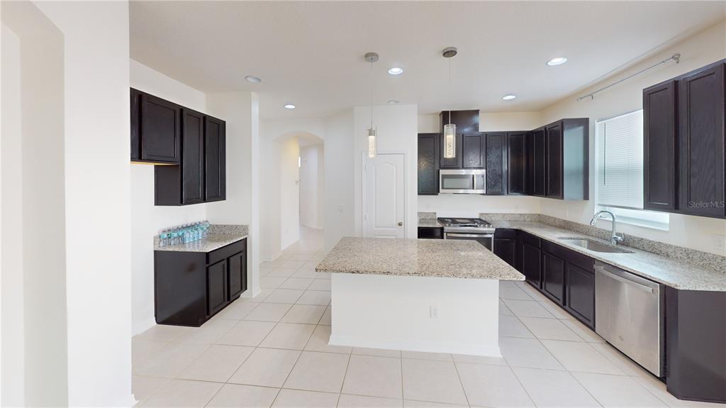 A kitchen features dark wood cabinets, granite countertops, a central island, and tile flooring — 8331 BAYLISS COURT, ORLANDO, FL
