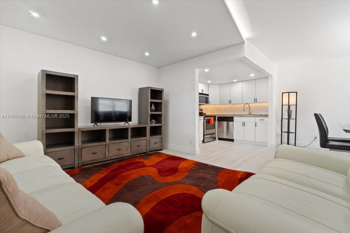A living room features a white sofa, a colorful rug, and an adjacent open kitchen — 590 Brittany M # 590, Delray Beach FL 33446, DELRAY BEACH, FL