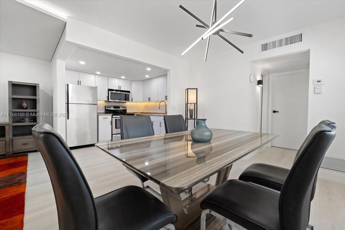 A dining area with a glass-topped table and chairs sits adjacent to a white kitchen — 590 Brittany M # 590, Delray Beach FL 33446, DELRAY BEACH, FL
