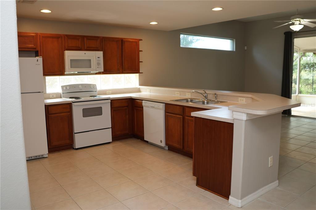 A kitchen features wood cabinets, white appliances, tile flooring, and a breakfast bar — 1730 TEALBRIAR AVENUE, OVIEDO, FL