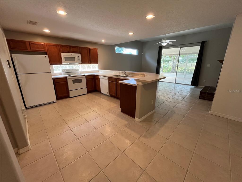 A kitchen with wood cabinets, white appliances, and tile flooring opens to a living area — 1730 TEALBRIAR AVENUE, OVIEDO, FL