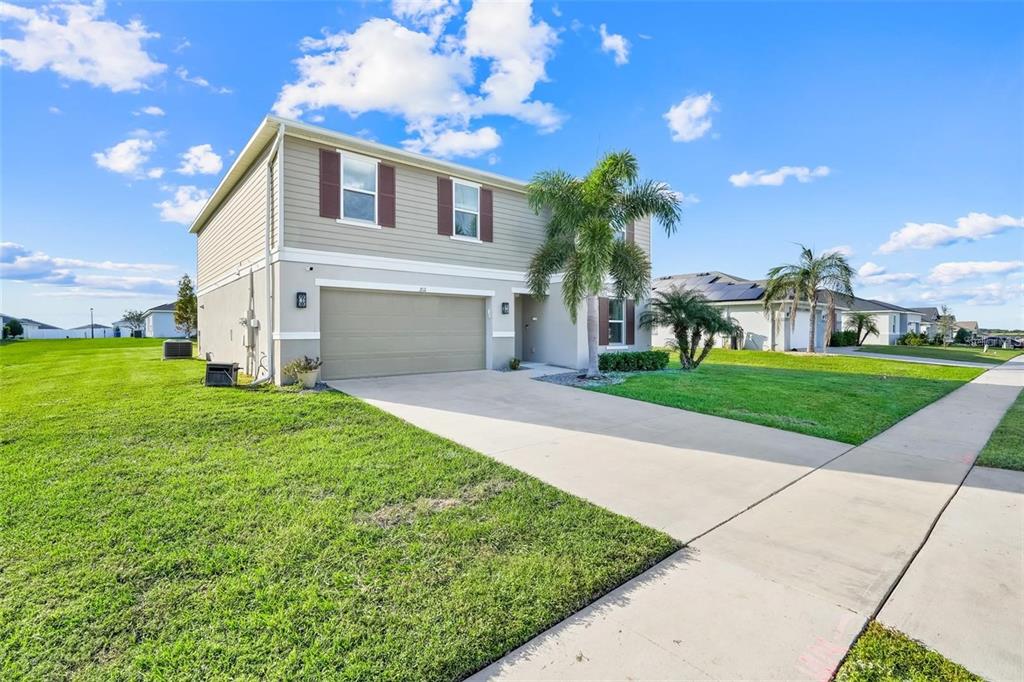 A two-story suburban house with a beige exterior, a two-car garage, and a palm tree — 2111 FICUS STREET, MASCOTTE, FL