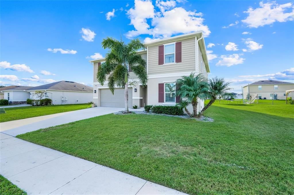 A two-story suburban house with a beige exterior, a two-car garage, and palm trees — 2111 FICUS STREET, MASCOTTE, FL