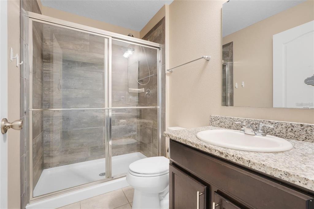 A bathroom features a glass-enclosed shower with wood-look tile, a toilet, and a granite vanity — 2111 FICUS STREET, MASCOTTE, FL