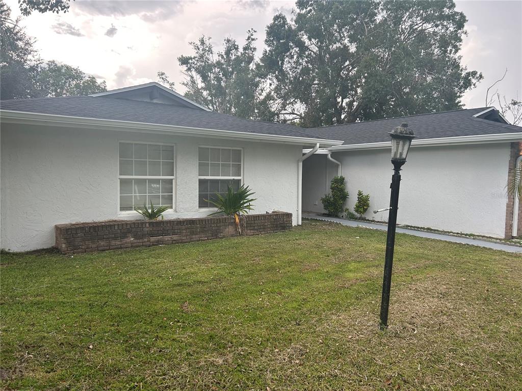 A white single-story house features a brick planter box, a lamp post, and a lawn — 620 MIDIRON DRIVE, KISSIMMEE, FL