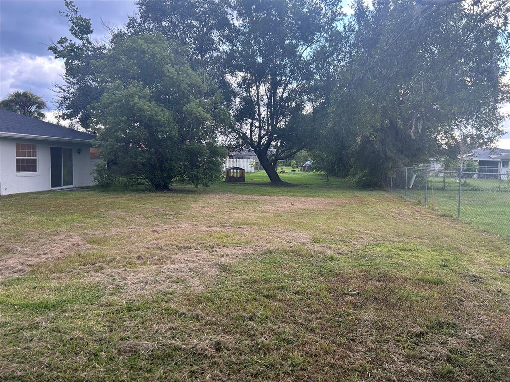 A grassy backyard features mature trees, a small shed, and a chain-link fence — 620 MIDIRON DRIVE, KISSIMMEE, FL
