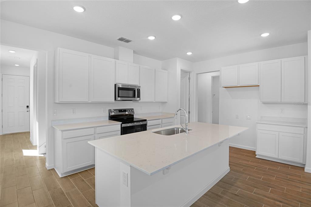 A modern kitchen features white cabinets, a central island with a sink, and wood-look flooring — 6183 SW 64TH TERRACE, OCALA, FL