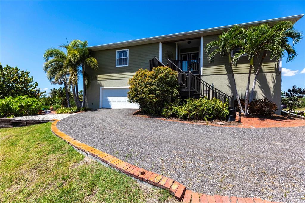 A two-story house with a gravel driveway, brick border, and palm trees in the yard — 3712 BALBOA COURT, PUNTA GORDA, FL