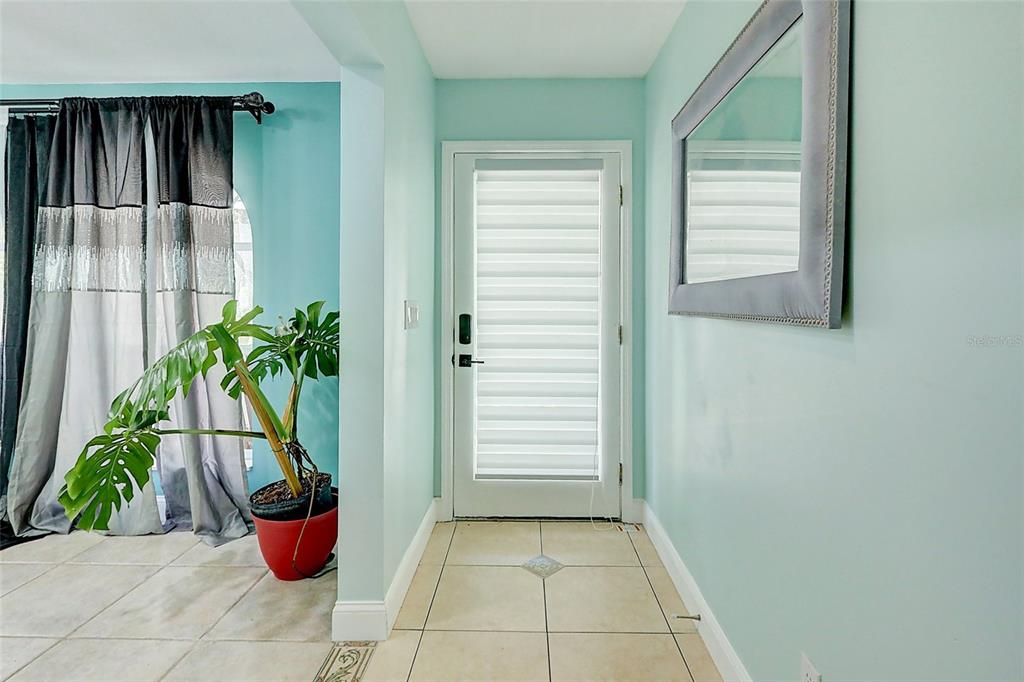 An entryway features light blue walls, tile flooring, a glass-paneled door, and a wall mirror — 238 SW GROVE AVENUE, PORT ST LUCIE, FL