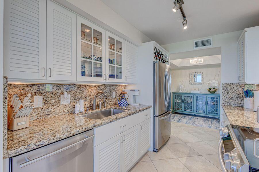 A kitchen featuring white louvered cabinets, granite countertops, stainless steel appliances, and tile flooring — 5550 N Ocean Drive # 3c, Riviera Beach FL 33404, RIVIERA BEACH, FL