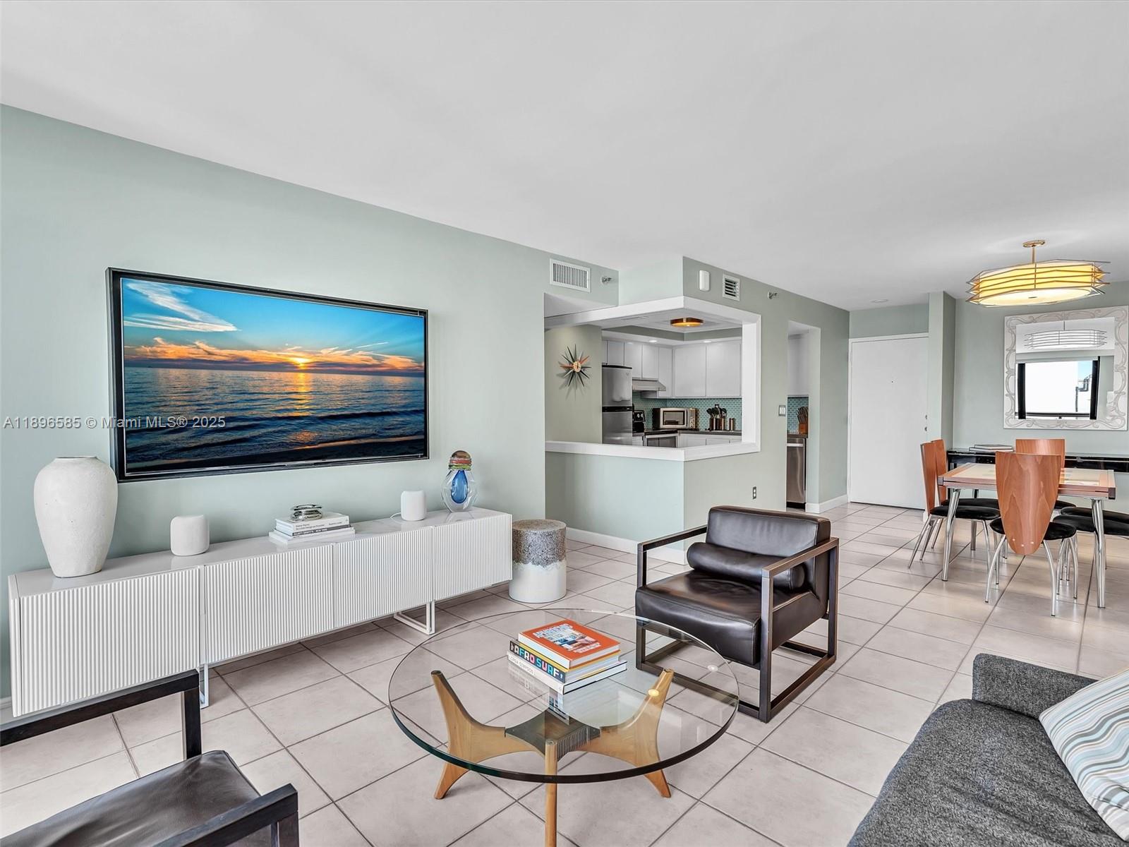 A living room with a wall-mounted television, white media console, and an open kitchen — 1775 Washington Ave # 8B, Miami Beach FL 33139, MIAMI BEACH, FL