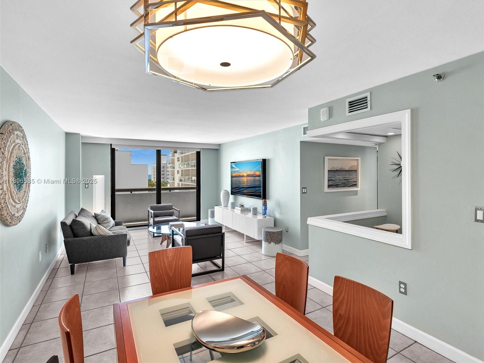 A living and dining area features light blue walls, tile flooring, and a modern chandelier — 1775 Washington Ave # 8B, Miami Beach FL 33139, MIAMI BEACH, FL