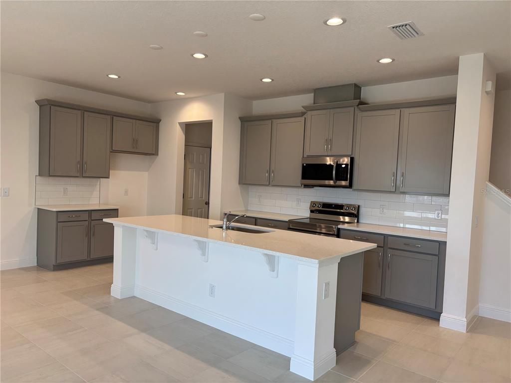 A modern kitchen features gray cabinets, white countertops, a central island, and stainless steel appliances — 1879 CHURCH LAKE STREET, GROVELAND, FL