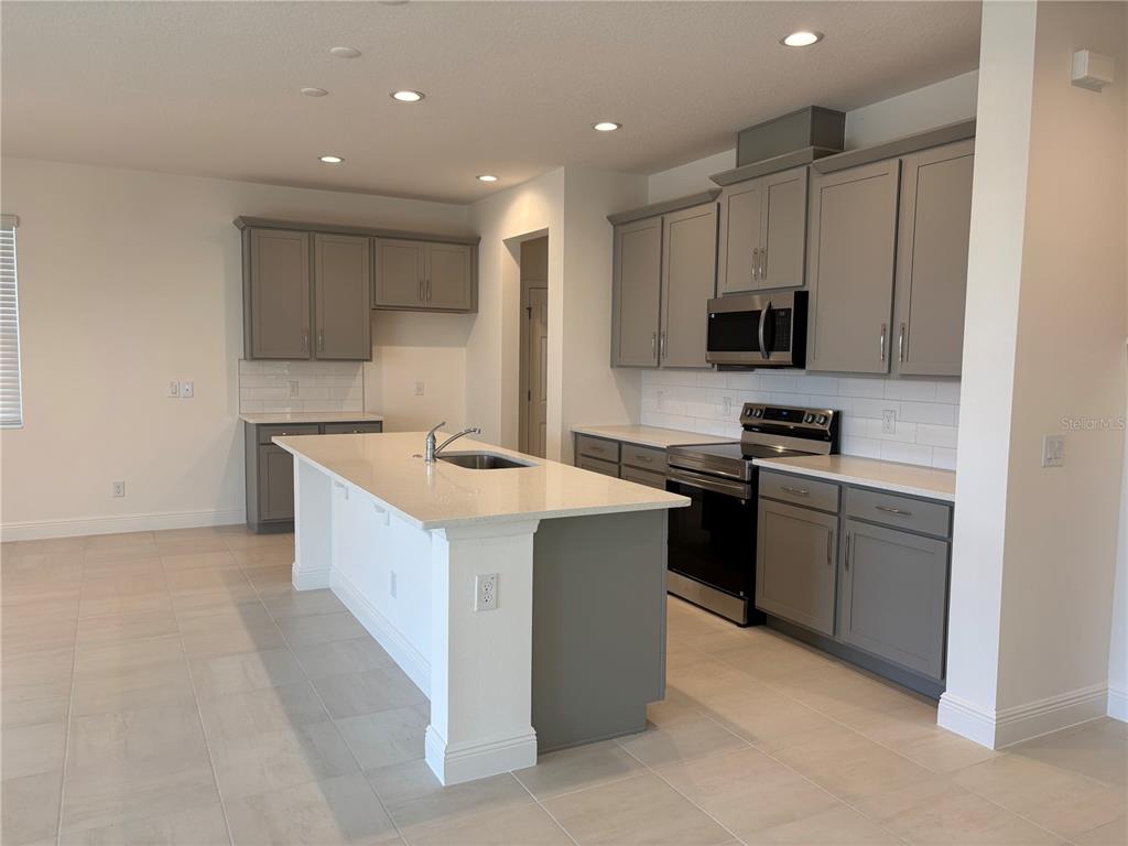 A modern kitchen features gray cabinets, white countertops, a central island, and stainless steel appliances — 1879 CHURCH LAKE STREET, GROVELAND, FL
