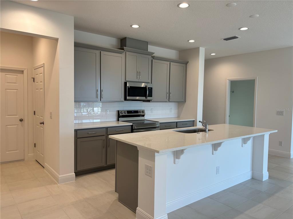 A kitchen features gray cabinets, white countertops, a center island, and stainless steel appliances — 1879 CHURCH LAKE STREET, GROVELAND, FL