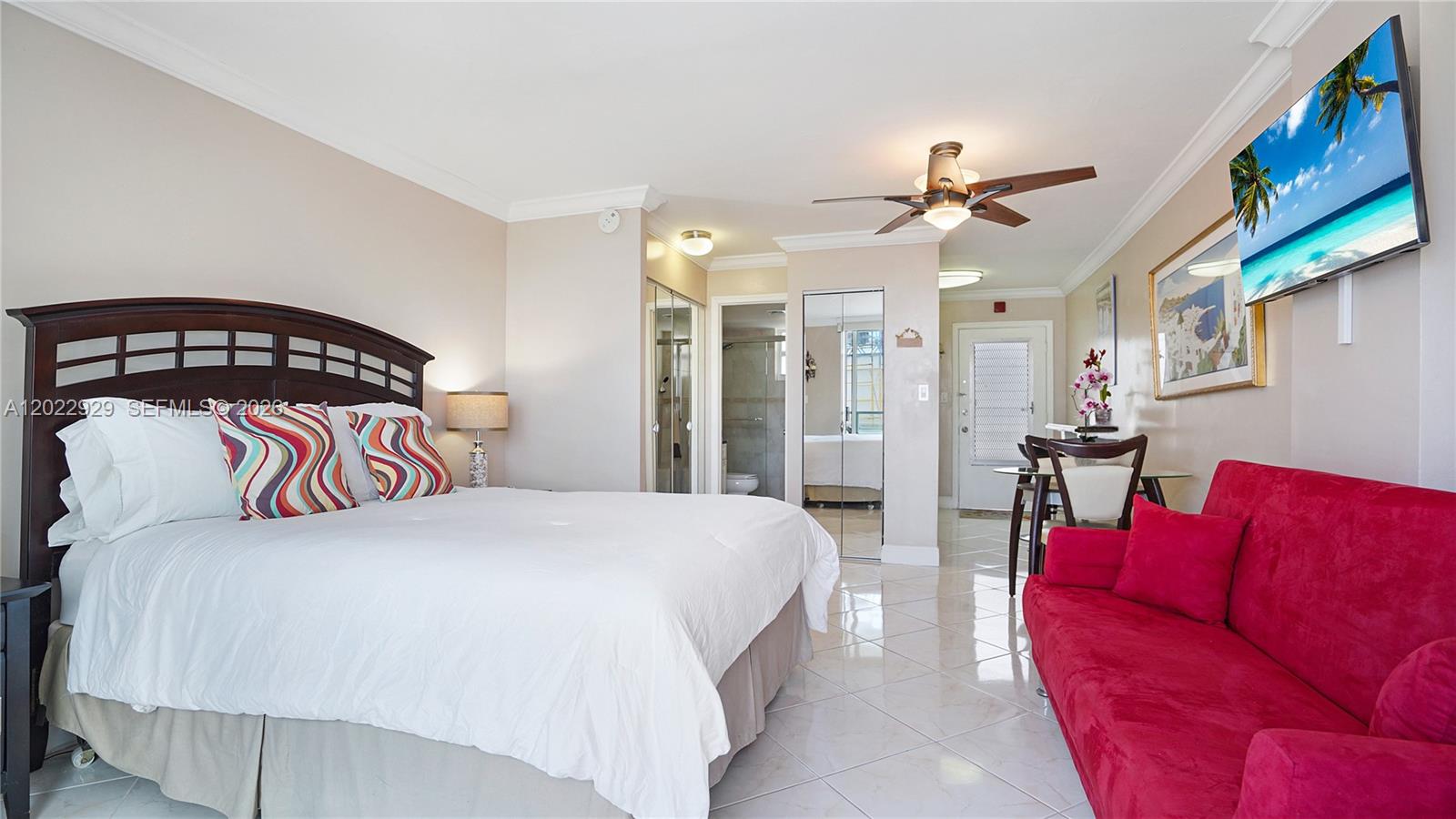 A bedroom features a bed, a red sofa, a dining set, and a wall-mounted television — 1750 James Ave # 9J, Miami Beach FL 33139, MIAMI BEACH, FL
