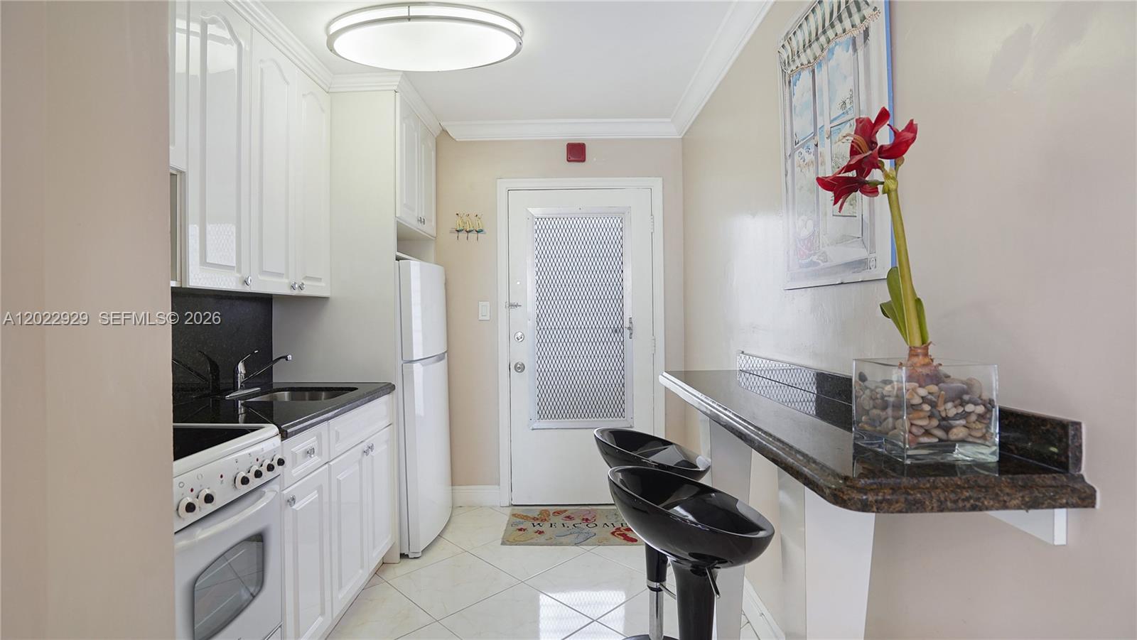 A small kitchen features white cabinets, black countertops, a breakfast bar, and a white door — 1750 James Ave # 9J, Miami Beach FL 33139, MIAMI BEACH, FL