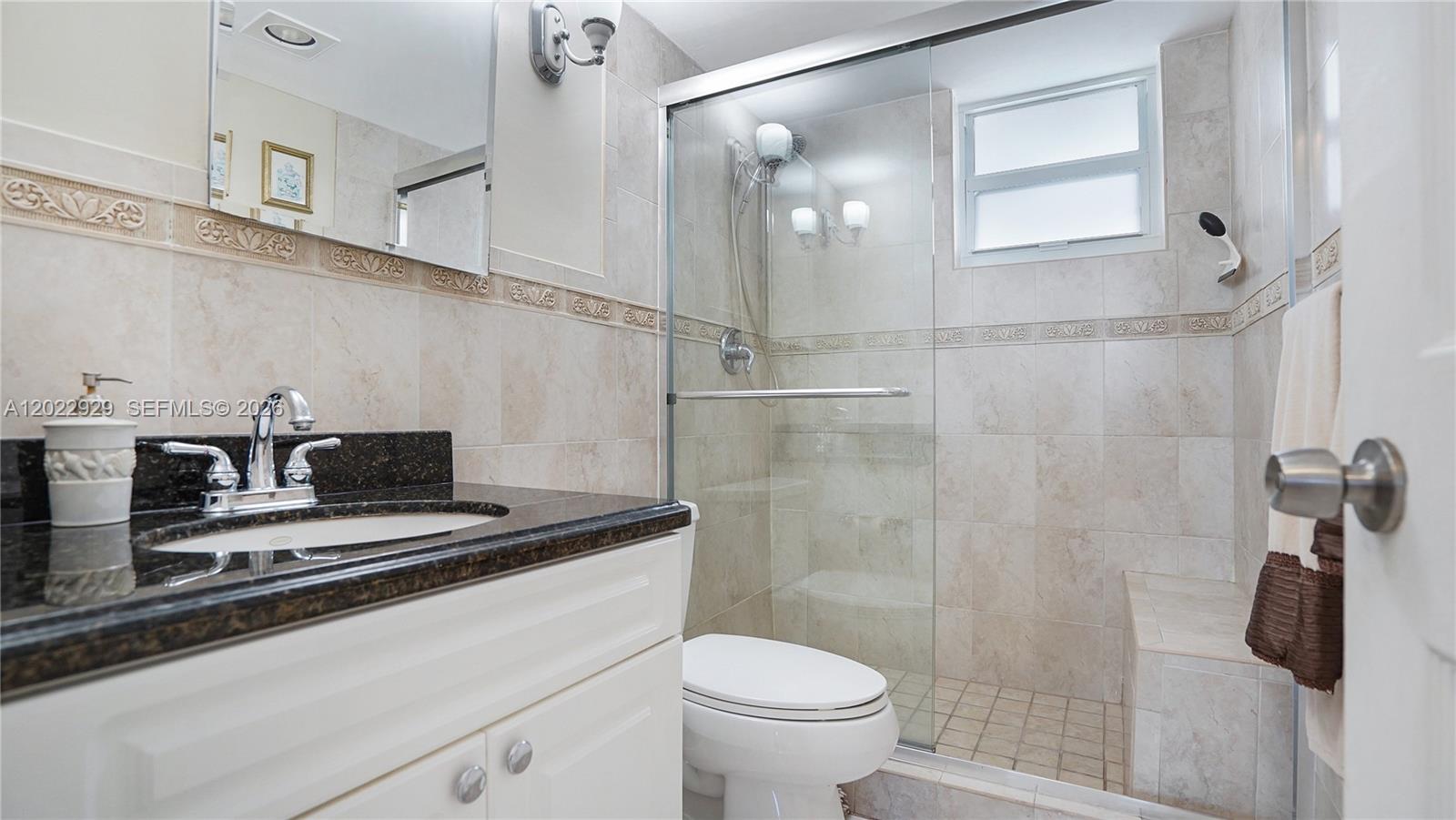 A bathroom features a white vanity with a dark countertop, a toilet, and a glass-enclosed shower — 1750 James Ave # 9J, Miami Beach FL 33139, MIAMI BEACH, FL