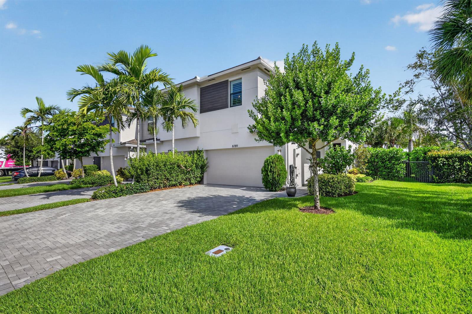 A two-story townhouse with a paved driveway, palm trees, and a green lawn — 8789 Antarus Drive, Lake Worth FL 33467, LAKE WORTH, FL