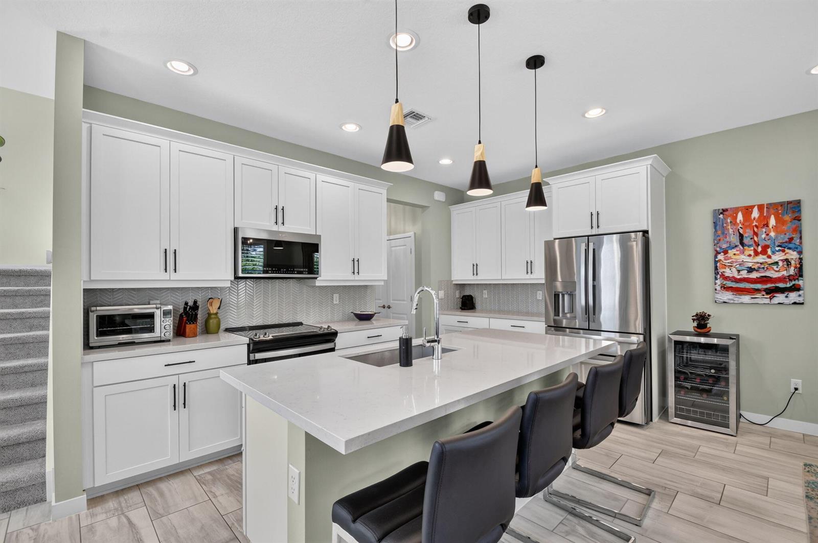 A modern kitchen features white cabinetry, a large quartz island with bar seating, and stainless appliances — 8789 Antarus Drive, Lake Worth FL 33467, LAKE WORTH, FL