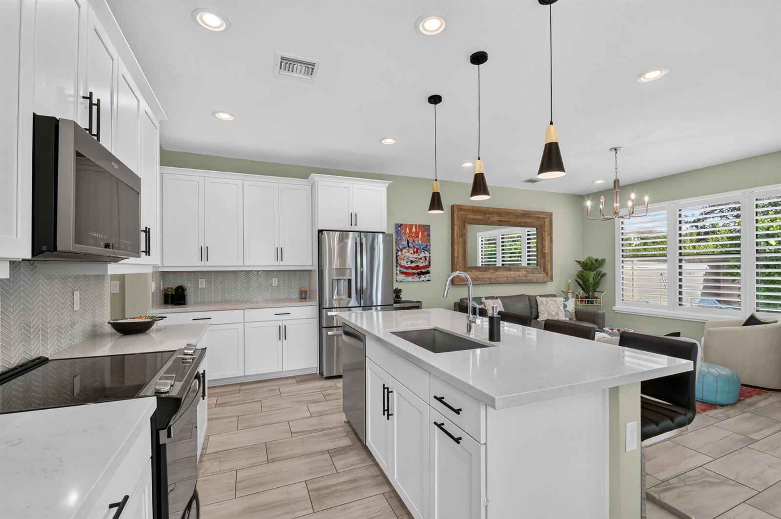 A modern kitchen features white cabinetry, quartz countertops, stainless steel appliances, and a central island — 8789 Antarus Drive, Lake Worth FL 33467, LAKE WORTH, FL