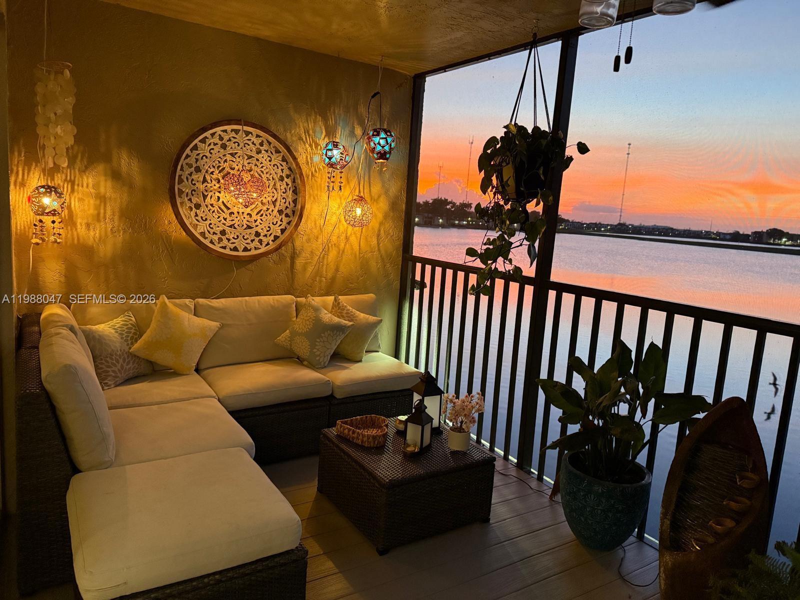 A screened-in balcony features wicker sectional seating, hanging lanterns, and a sunset water view — 605 Ives Dairy Rd # 7, Miami FL 33179, MIAMI, FL