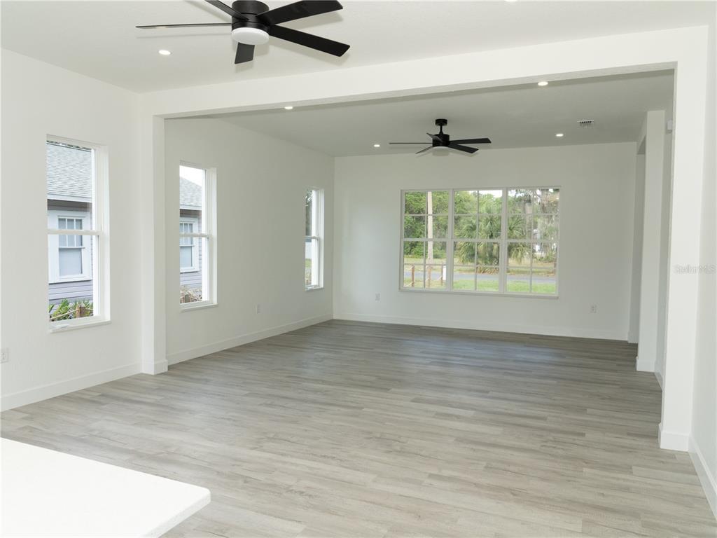 A spacious, unfurnished living area features white walls, light wood-look flooring, and two ceiling fans — 1115 HICKORY, SANFORD, FL