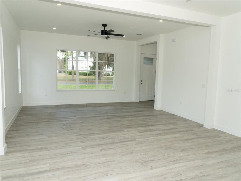An empty room features light wood-look flooring, white walls, a ceiling fan, and large windows — 1115 HICKORY, SANFORD, FL