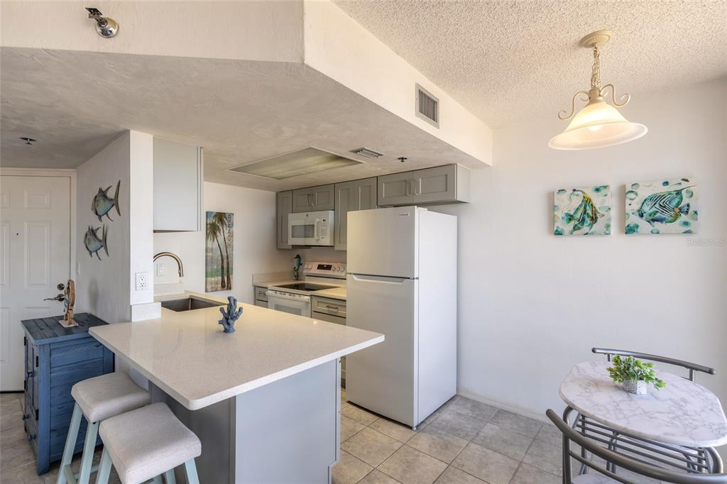 A kitchen features a white breakfast bar, gray cabinets, a white refrigerator, and tile flooring — 3023 S ATLANTIC AVENUE UNIT 9010, DAYTONA BEACH, FL