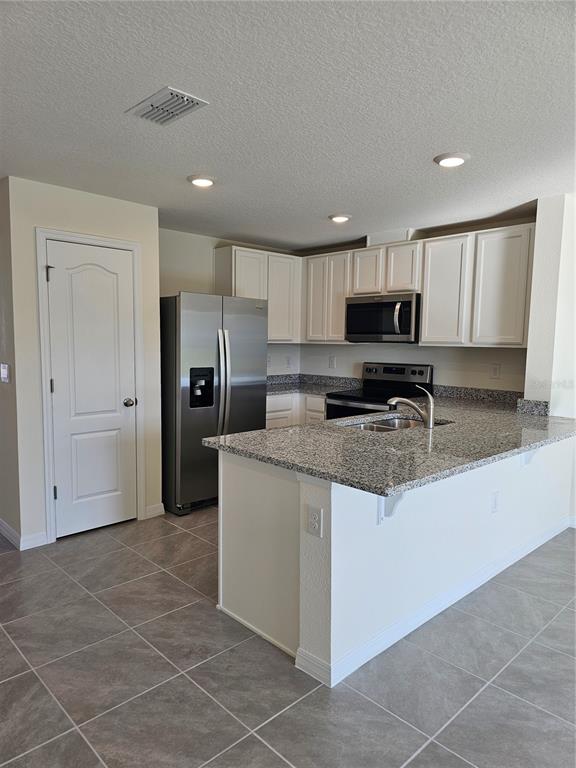 A kitchen features white cabinets, granite countertops, stainless steel appliances, and gray tile flooring — 2926 HUDSON HAMMOCK WAY, BEND, HARMONY, FL