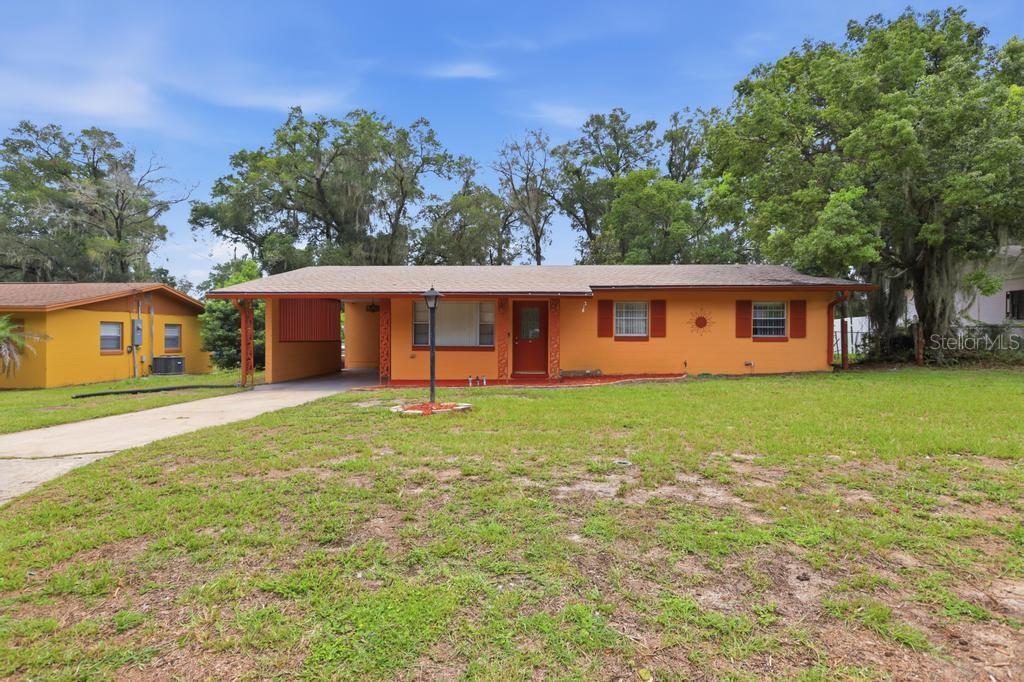 A single-story orange house features a carport, a red front door, and mature trees — 812 W FRANKLIN AVENUE, DELAND, FL