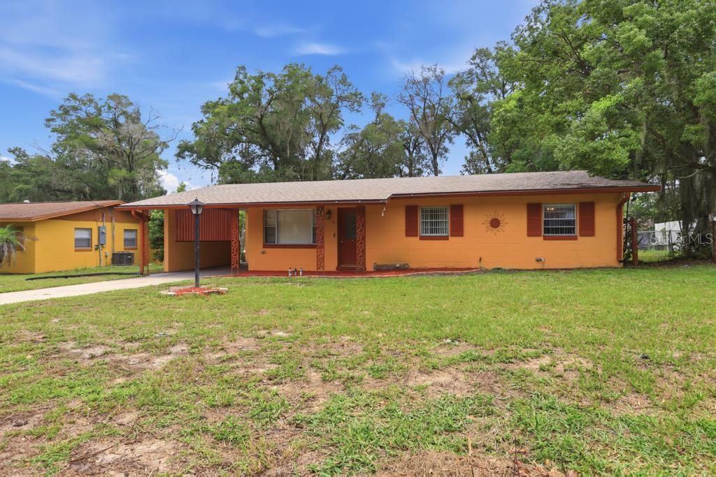 A single-story orange house with a carport, brown shutters, and a large front lawn — 812 W FRANKLIN AVENUE, DELAND, FL
