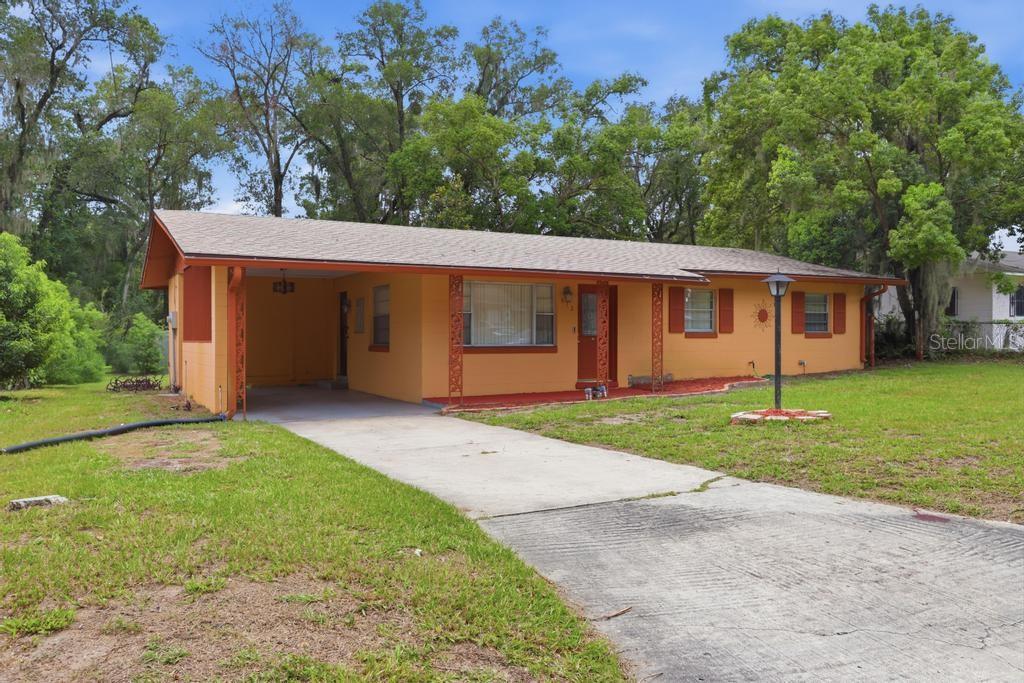 A single-story orange house with a carport, concrete driveway, and a large grassy yard — 812 W FRANKLIN AVENUE, DELAND, FL