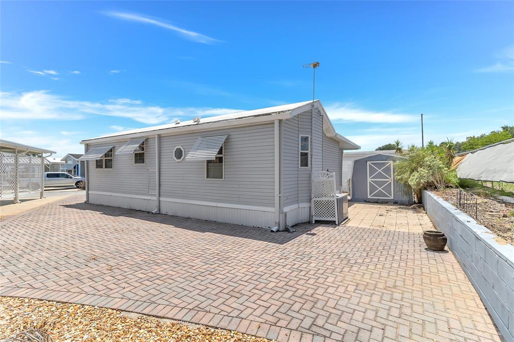 The exterior of a light gray mobile home features a brick paver patio and shed — 300 SKY CREST LOOP, DAVENPORT, FL