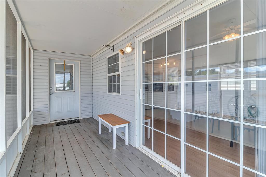 A covered porch with gray wood decking, light blue siding, a door, and sliding glass doors — 300 SKY CREST LOOP, DAVENPORT, FL