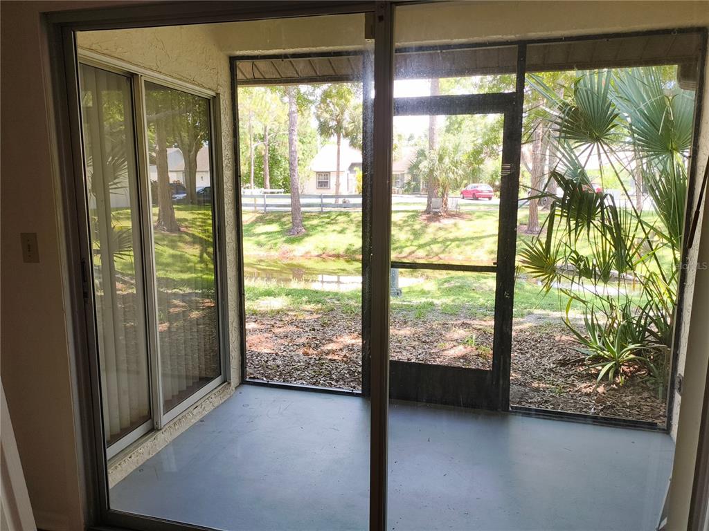 This virtually staged living room features a grey sofa, blue armchairs, and a sliding glass door — 3962 LA COSTA LANE, LARGO, FL