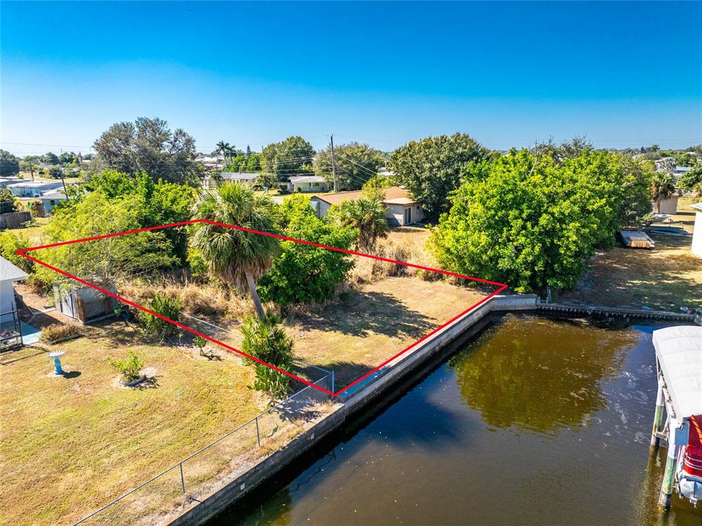 An aerial view shows a vacant waterfront lot outlined in red next to a canal — 21280 HIGGS DRIVE, PORT CHARLOTTE, FL