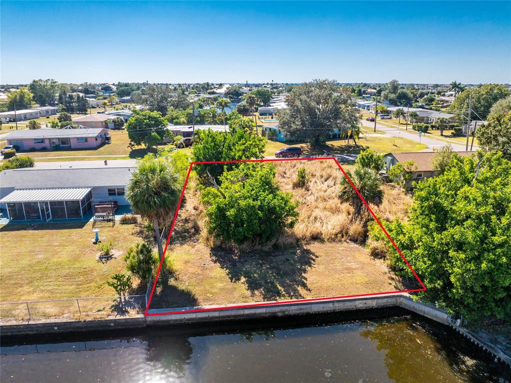 An aerial view shows a vacant waterfront lot outlined in red next to a house — 21280 HIGGS DRIVE, PORT CHARLOTTE, FL
