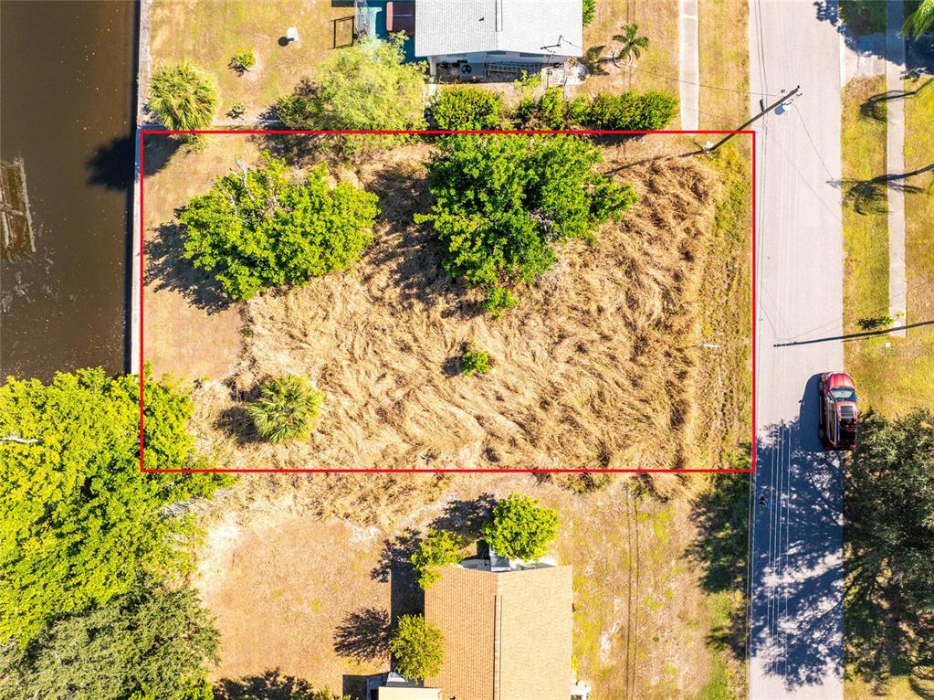 An aerial view shows a rectangular, grass-covered vacant lot situated between a canal and road — 21280 HIGGS DRIVE, PORT CHARLOTTE, FL