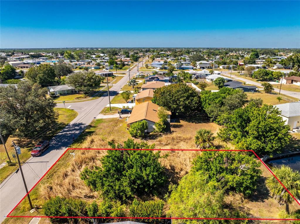 An aerial view shows a vacant, tree-covered residential lot outlined in red next to a canal — 21280 HIGGS DRIVE, PORT CHARLOTTE, FL