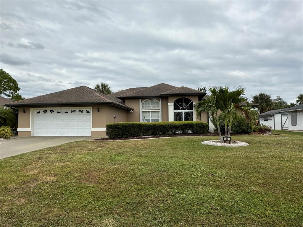A single-story house with a two-car garage, tan stucco exterior, and a front lawn — 1238 YORKSHIRE STREET, PORT CHARLOTTE, FL