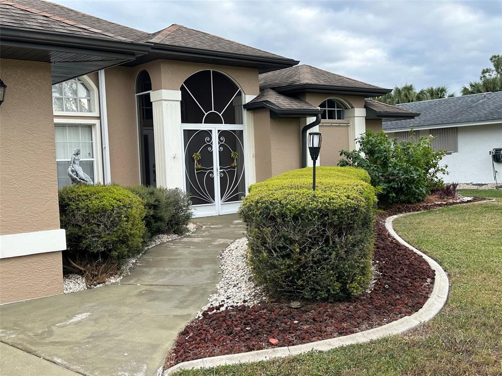 The exterior of a tan house features a screened front entryway and landscaped garden beds — 1238 YORKSHIRE STREET, PORT CHARLOTTE, FL